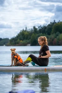 Person paddelt mit Moai 10'6 SUP-Board und Hund auf dem Wasser